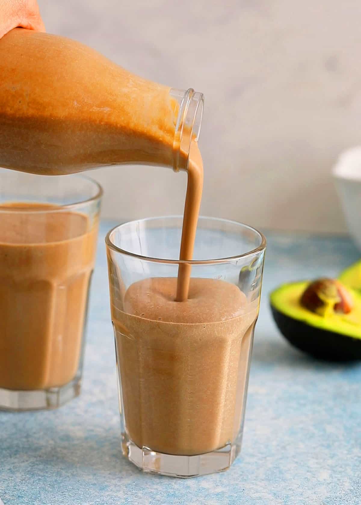 a hand pouring avocado smoothie into a glass.