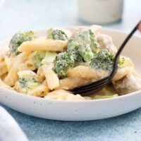 pasta, chicken and broccoli in a white round plate with black fork.
