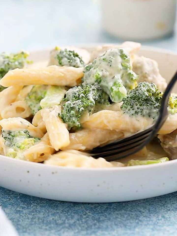 pasta, chicken and broccoli in a white round plate with black fork.