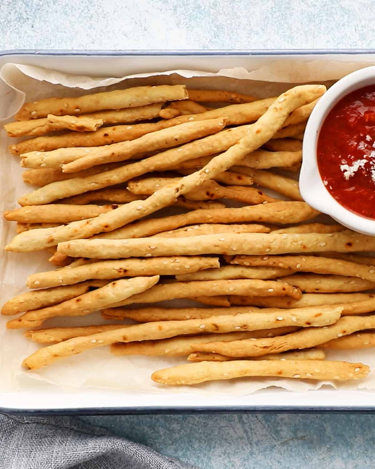 long thin breadsticks in a white tray along with red sauce in a small white bowl.