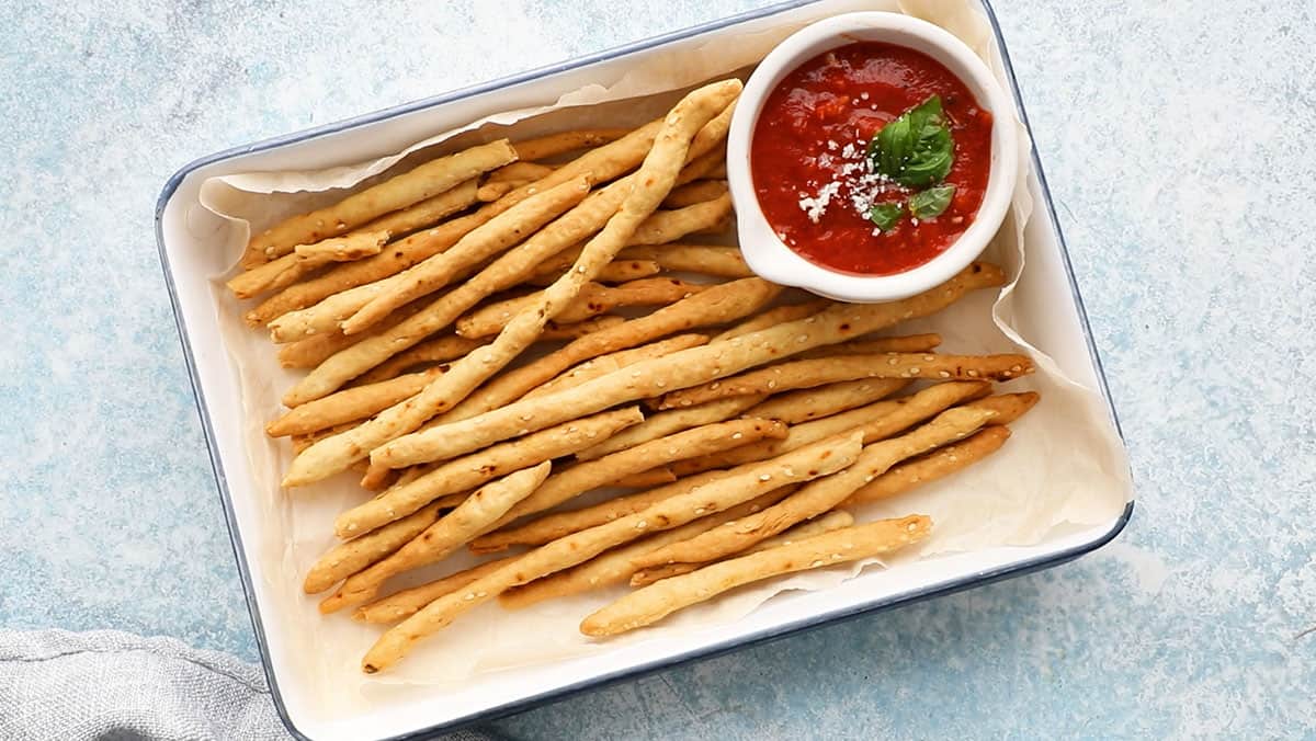 long thin breadsticks in a white tray along with red sauce in a small white bowl.