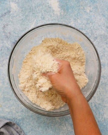 a hand mixing white flour in a glass bowl.