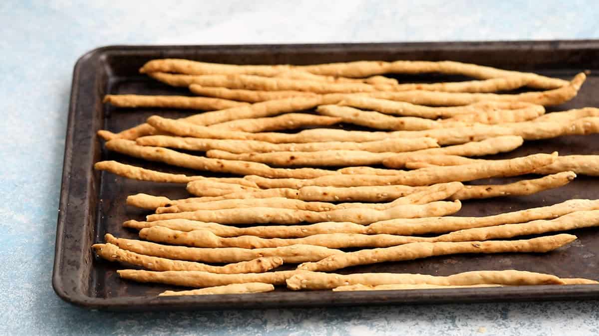 baked long breadsticks placed on a black cooking sheet.