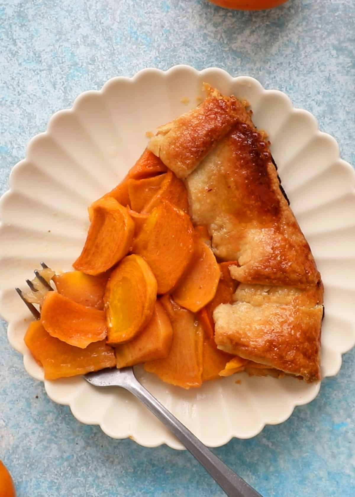 one slice of persimmon galette placed on a white scalopped plate.