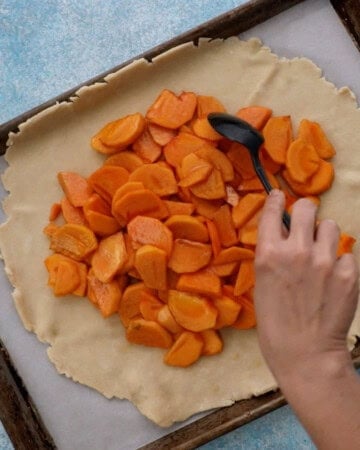 a hand placing sliced orange persimmons over rolled pie crust.