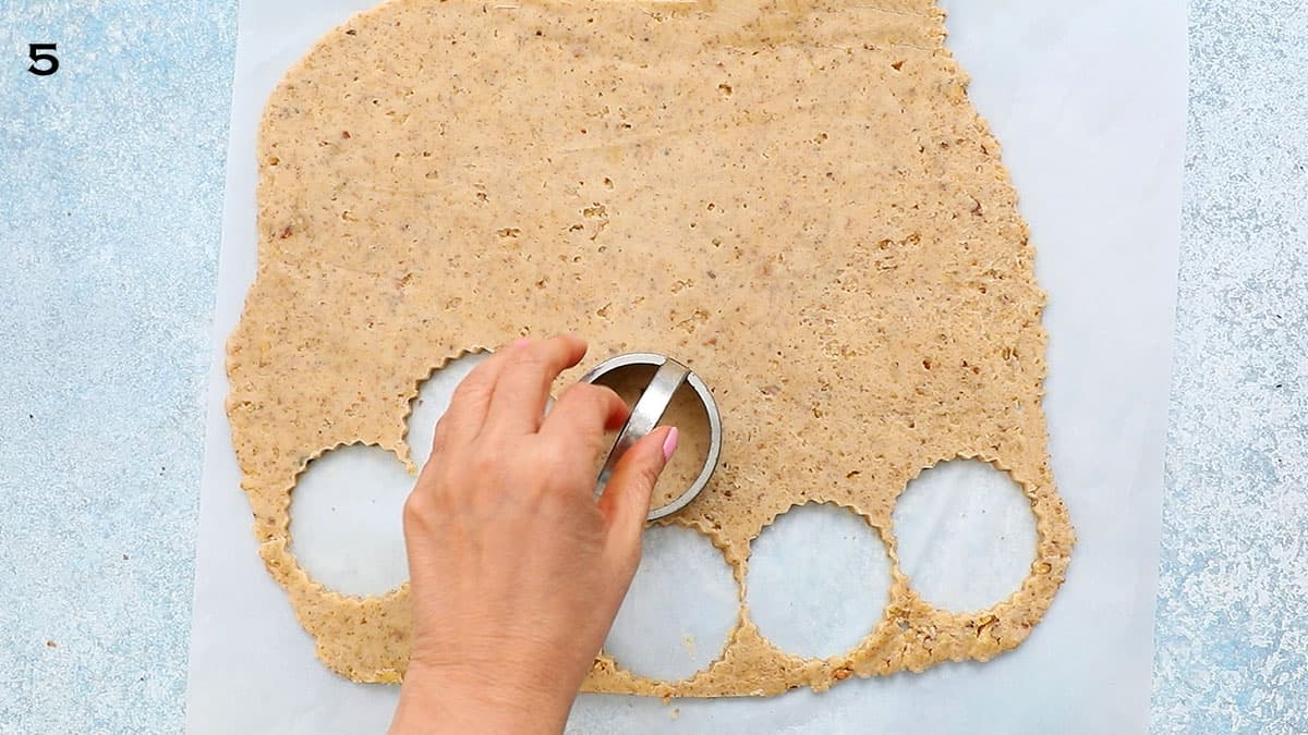 a hand punching out cookie dough using a fluted round cookie cutter.