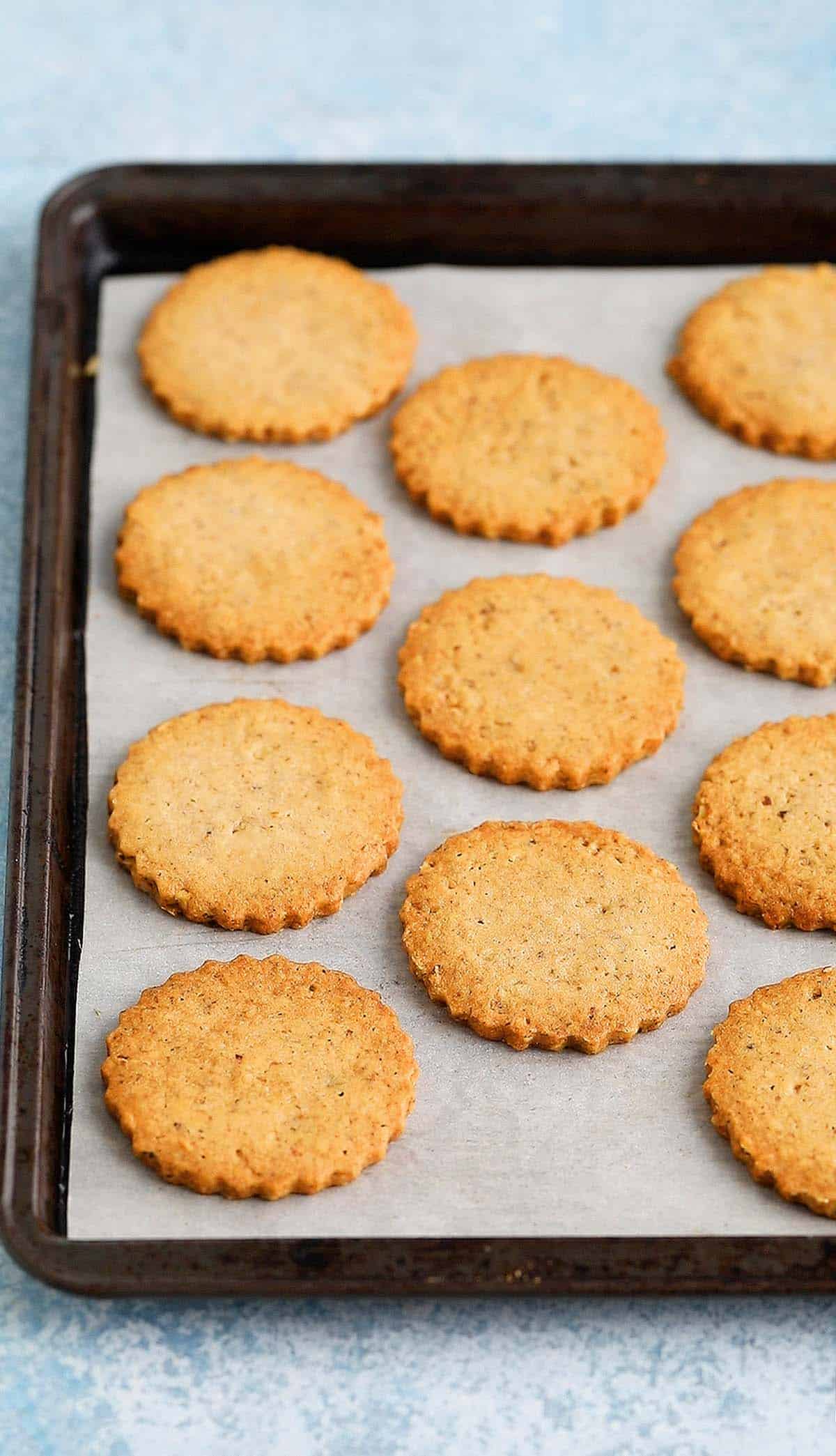 parchment lined black metal baking sheet filled with baked walnut cookies.