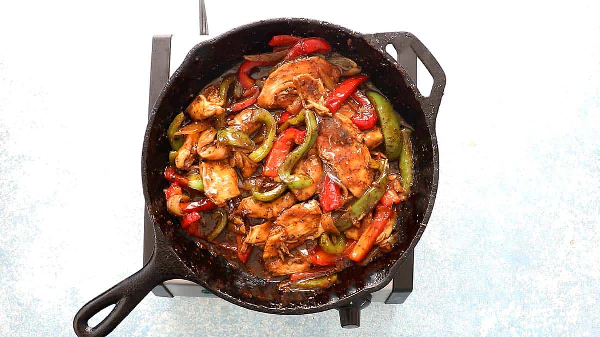 cooked black pepper chicken stir fry in a black skillet placed on a stove.