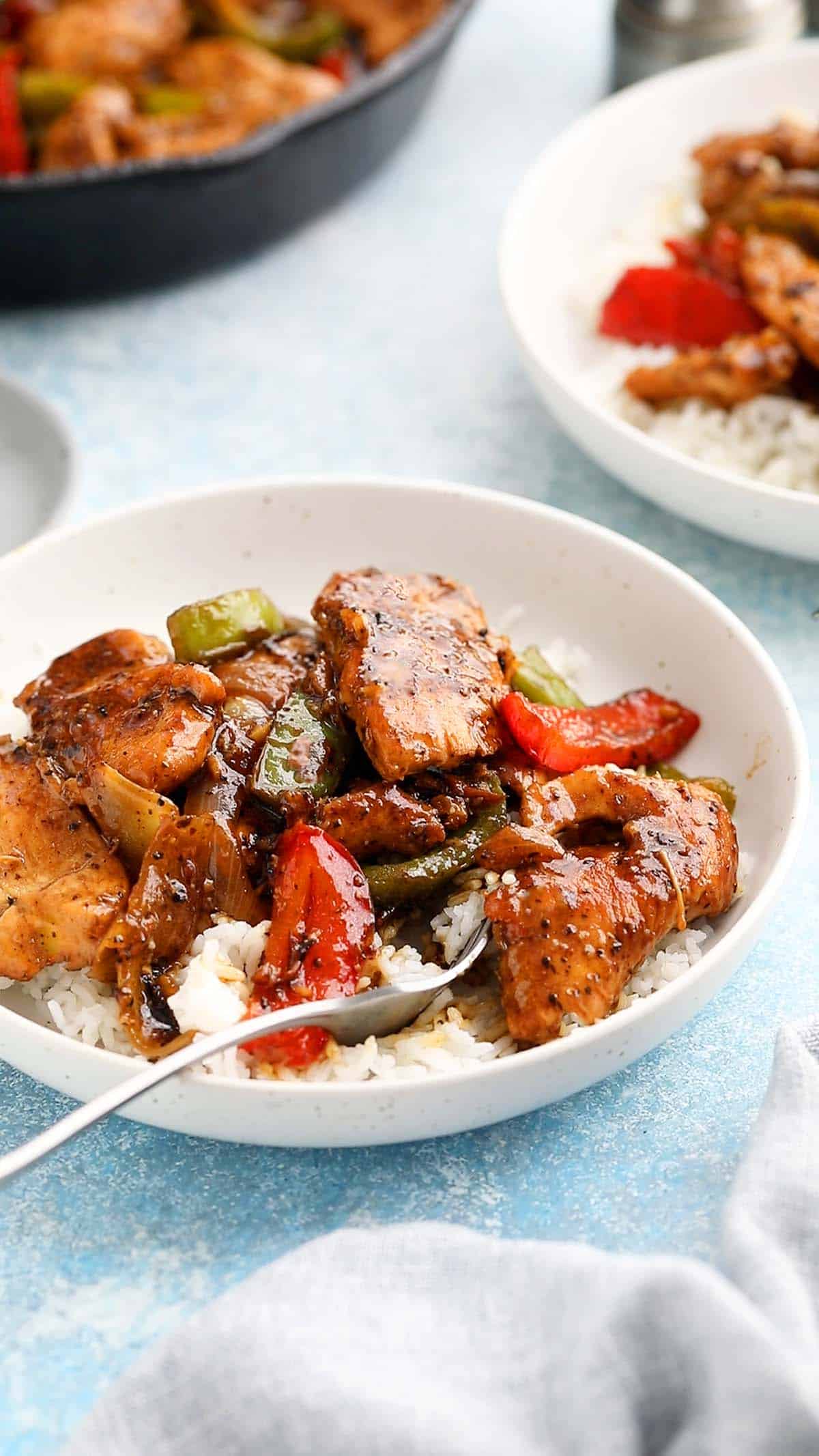 black pepper chicken stir fry over white rice in a round white bowl and fork.