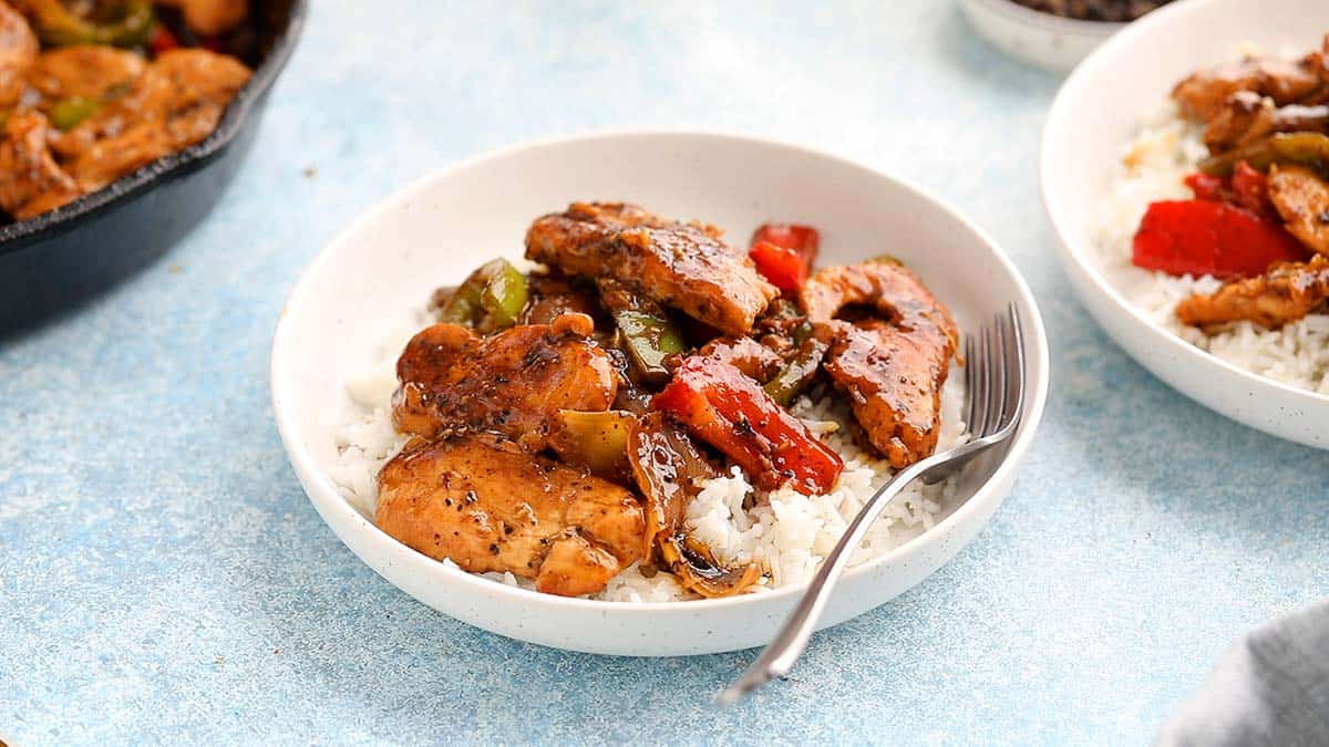 black pepper chicken stir fry over white rice in a round white bowl.