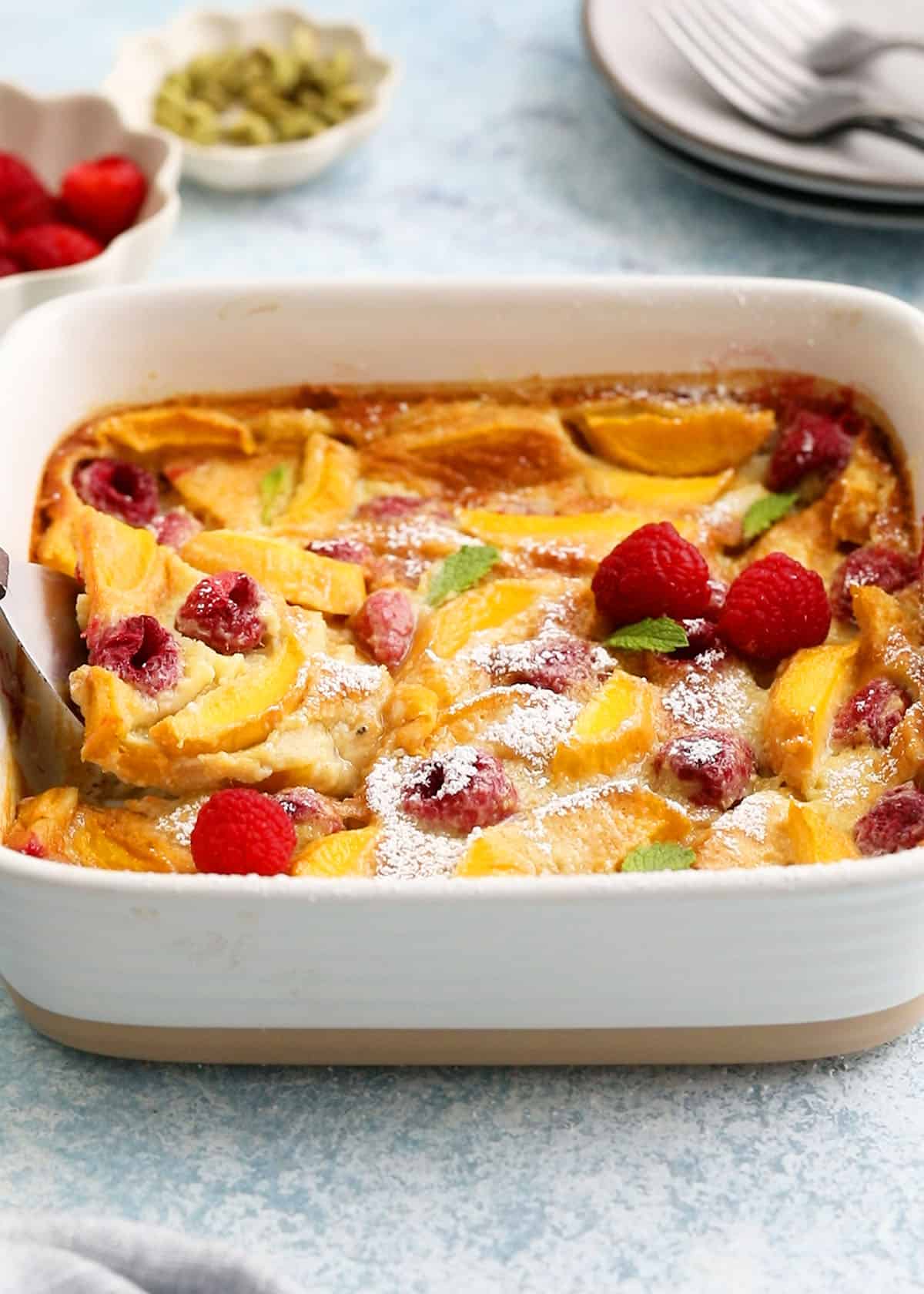 yellow clafoutis topped with red raspberries in a square baking dish.