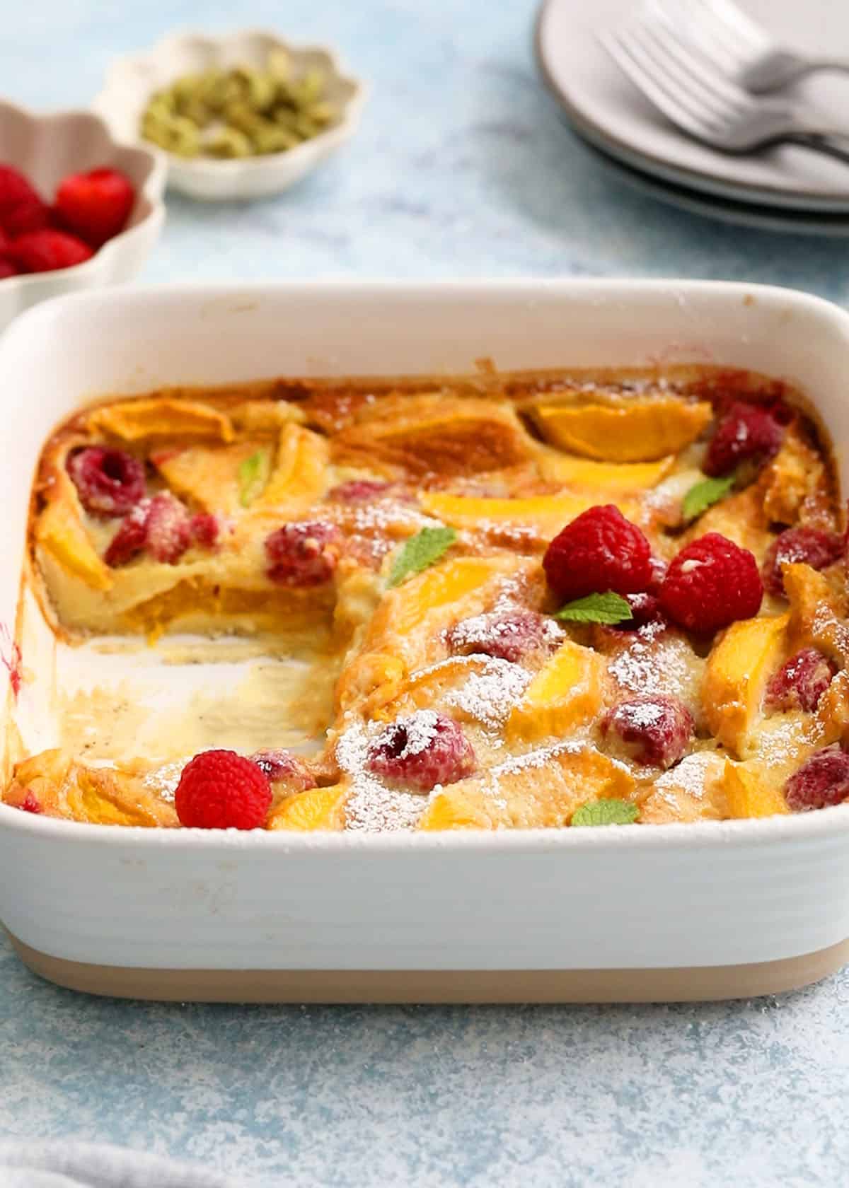 yellow clafoutis topped with red raspberries in a square baking dish.