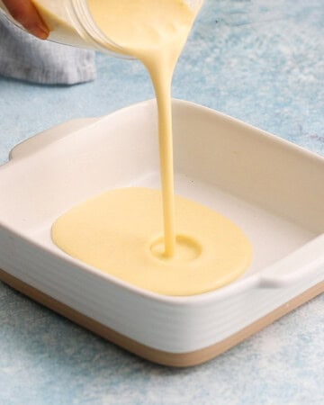 a hand pouring clafoutis batter into a square baking dish.