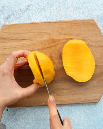 two hands cutting a mango into two halves.
