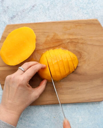 two hands slicing a mango half into slices.