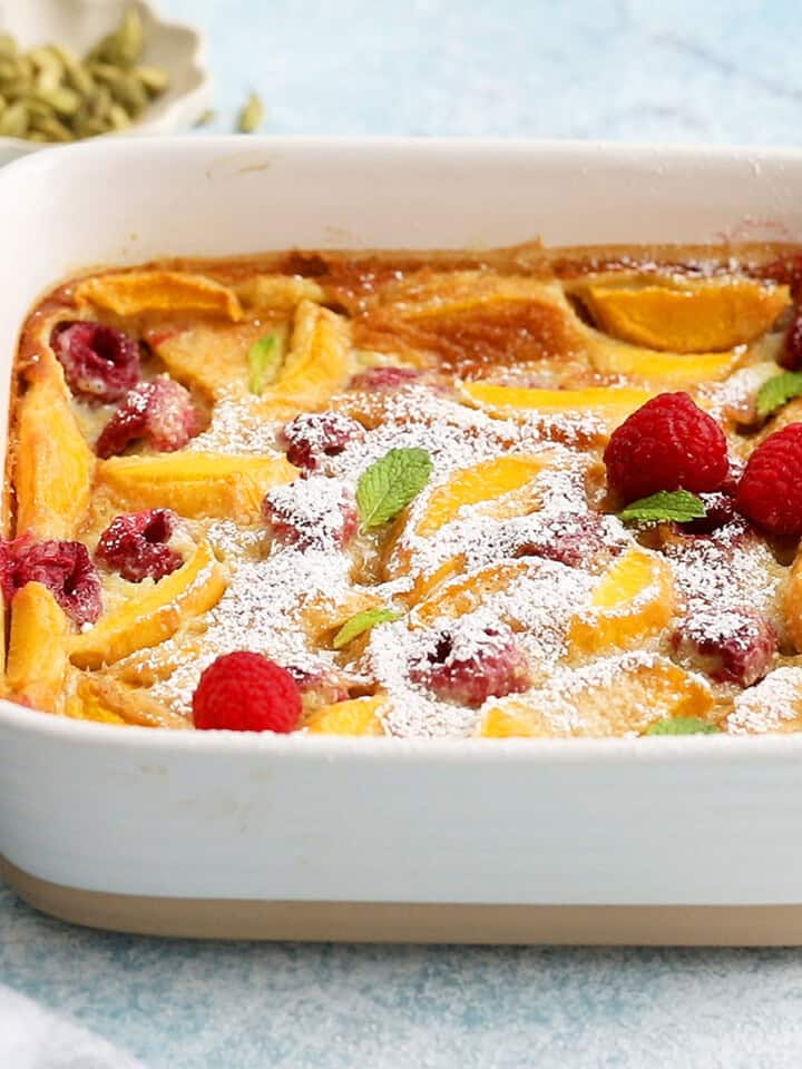 yellow clafoutis topped with red raspberries in a square baking dish.