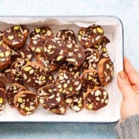 a hand holding a white rectangular tray filled with chocolate salami slices.