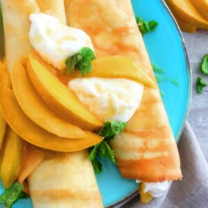 blue plate with 2 rolled crepes topped with sliced mangoes.