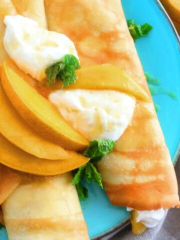 blue plate with 2 rolled crepes topped with sliced mangoes.