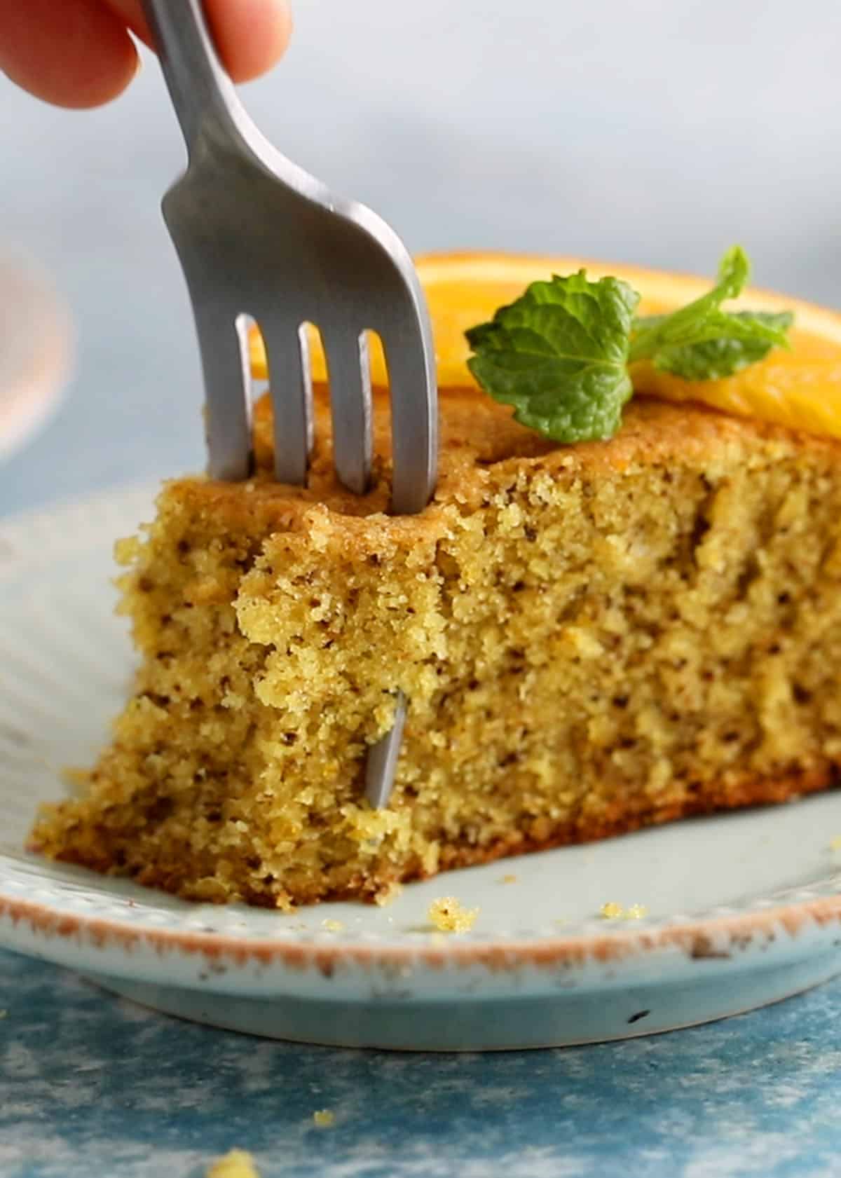 a metal fork cutting through a slice of brown cake slice placed on a green plate.