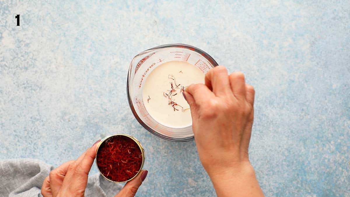 two hands adding saffron into a glass measuring cup. 