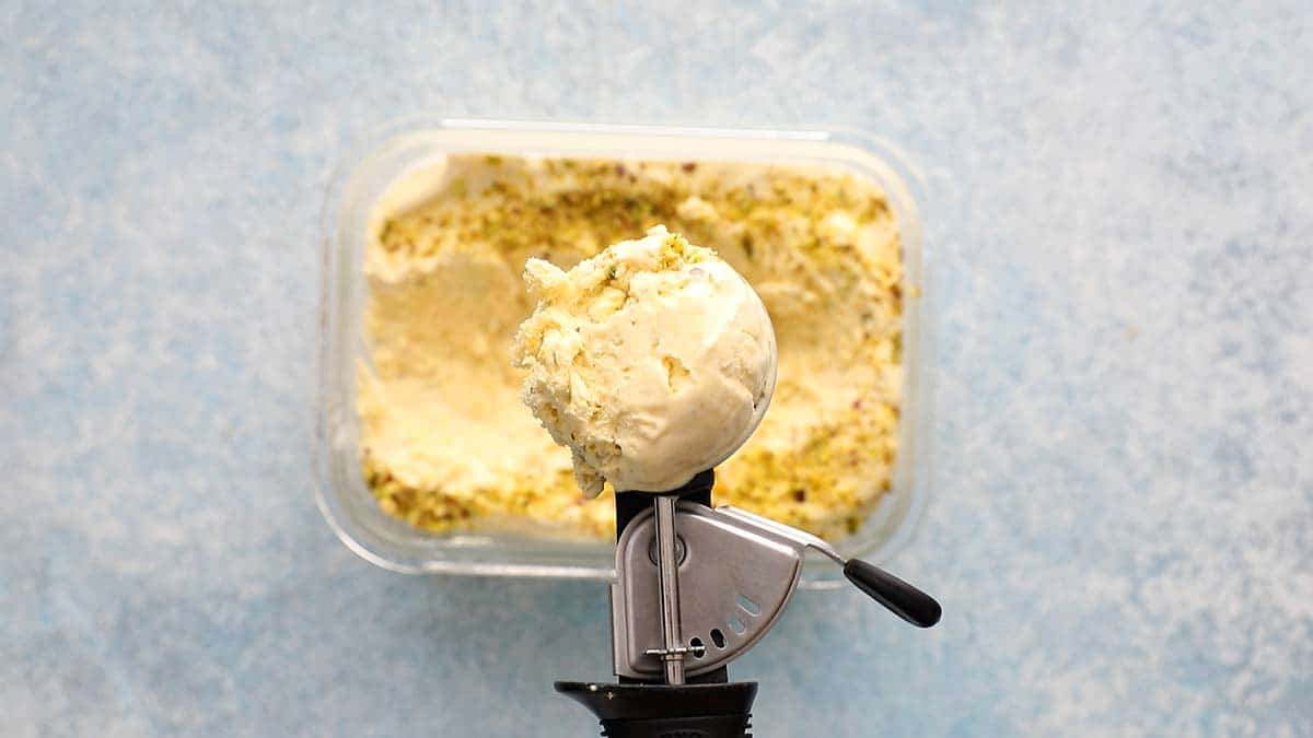 an ice cream scoop with kulfi above a glass dish filled with the same.
