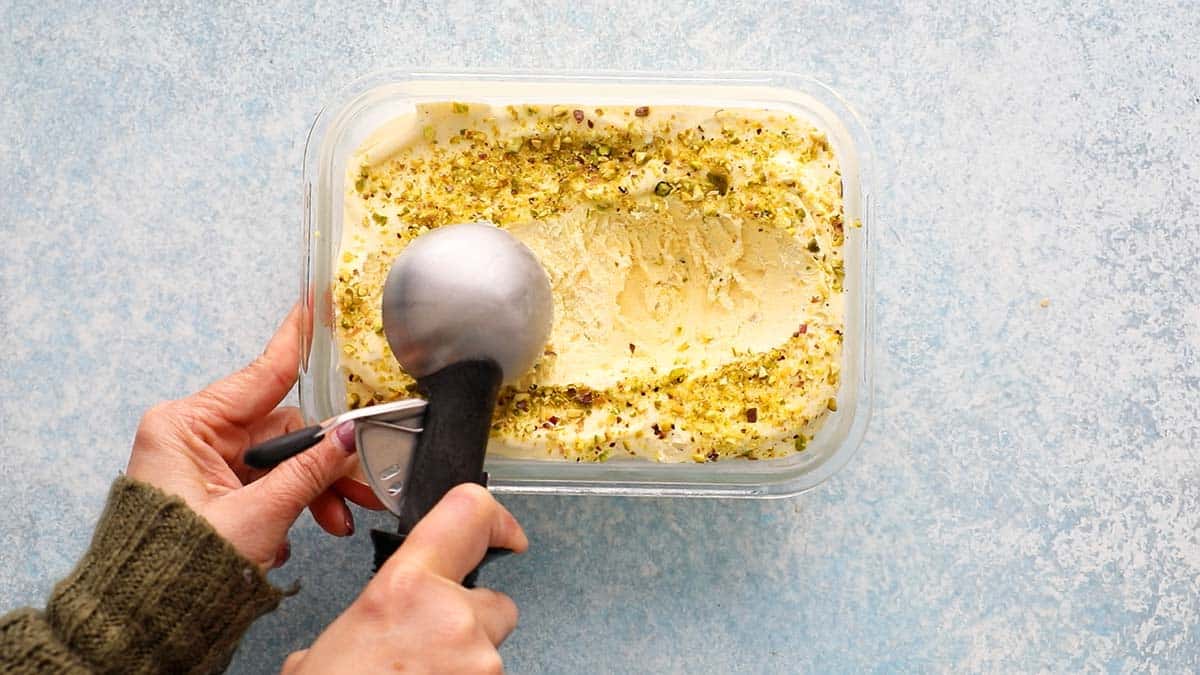 2 hands scooping kulfi ice cream with a ice cream scoop from a rectangle dish.