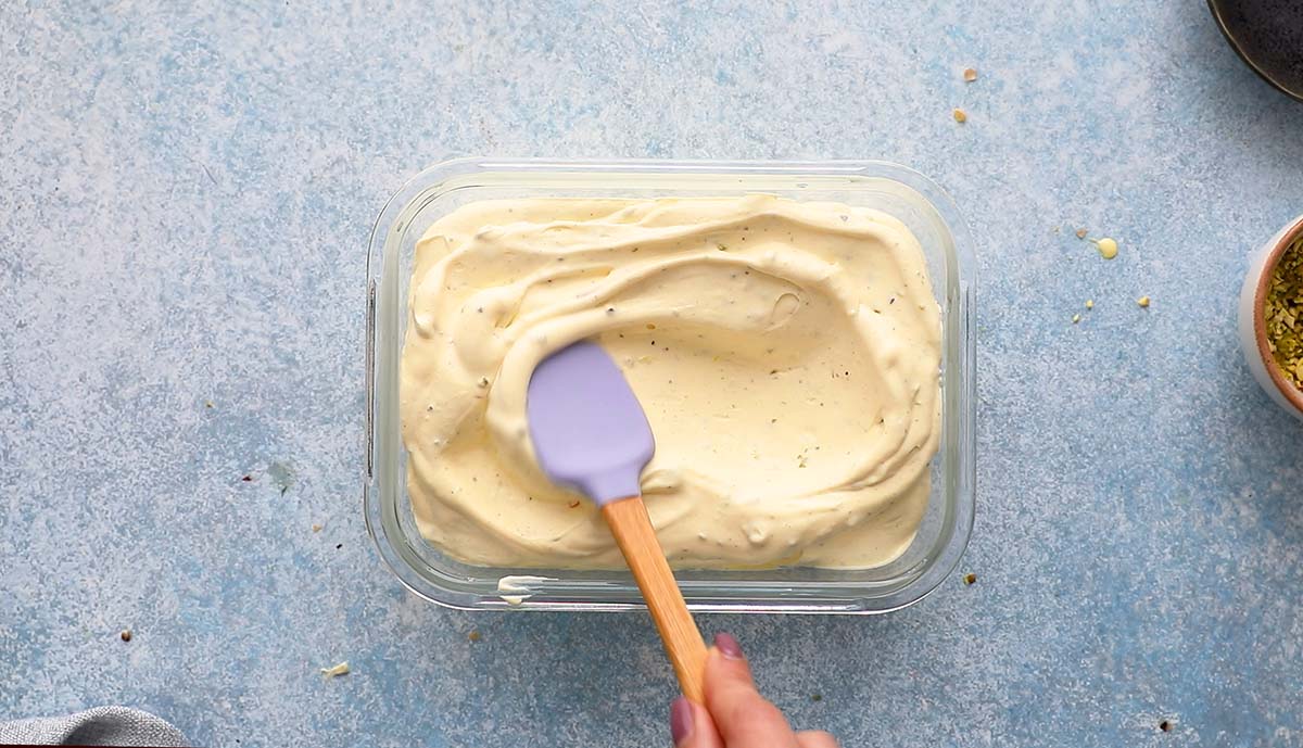 kulfi ice cream mixture being spread in a rectangle glass dish with a purple rubber spatula. 