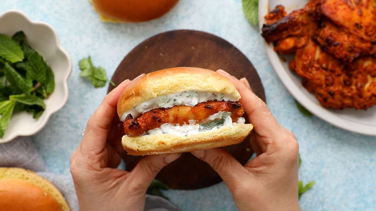 two hands holding one spicy tandoori chicken sandwich.