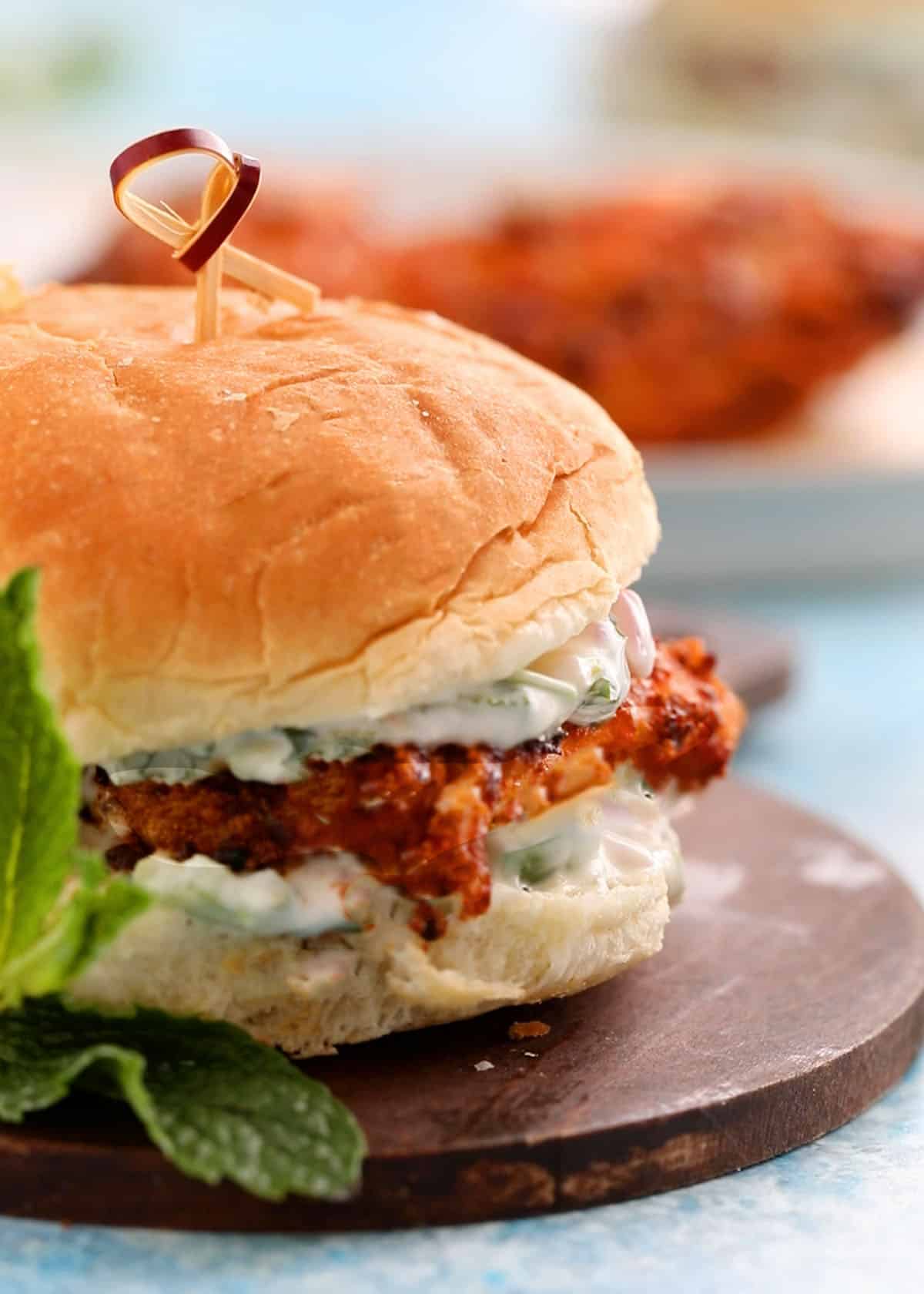 one spicy tandoori chicken sandwich placed on a brown board.
