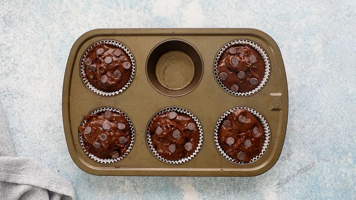 brown chocolate muffin batter in a metal muffin pan.