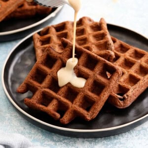 white sauce being poured on top of three dark brown chocolate waffles.