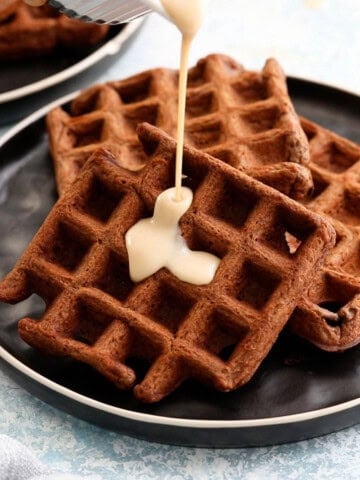white sauce being poured on top of three dark brown chocolate waffles.