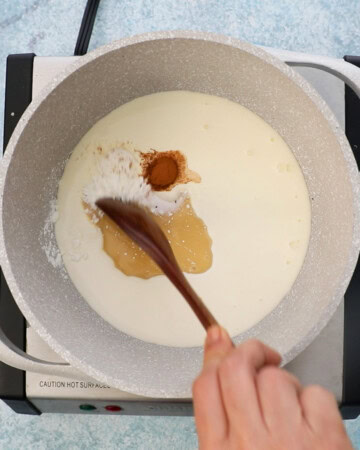 a hand mixing white milk along with cinnamon in a white saucepan.