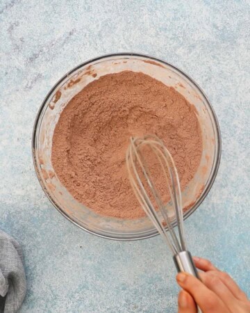 a hand whisking brown flour mixture in a glass bowl.