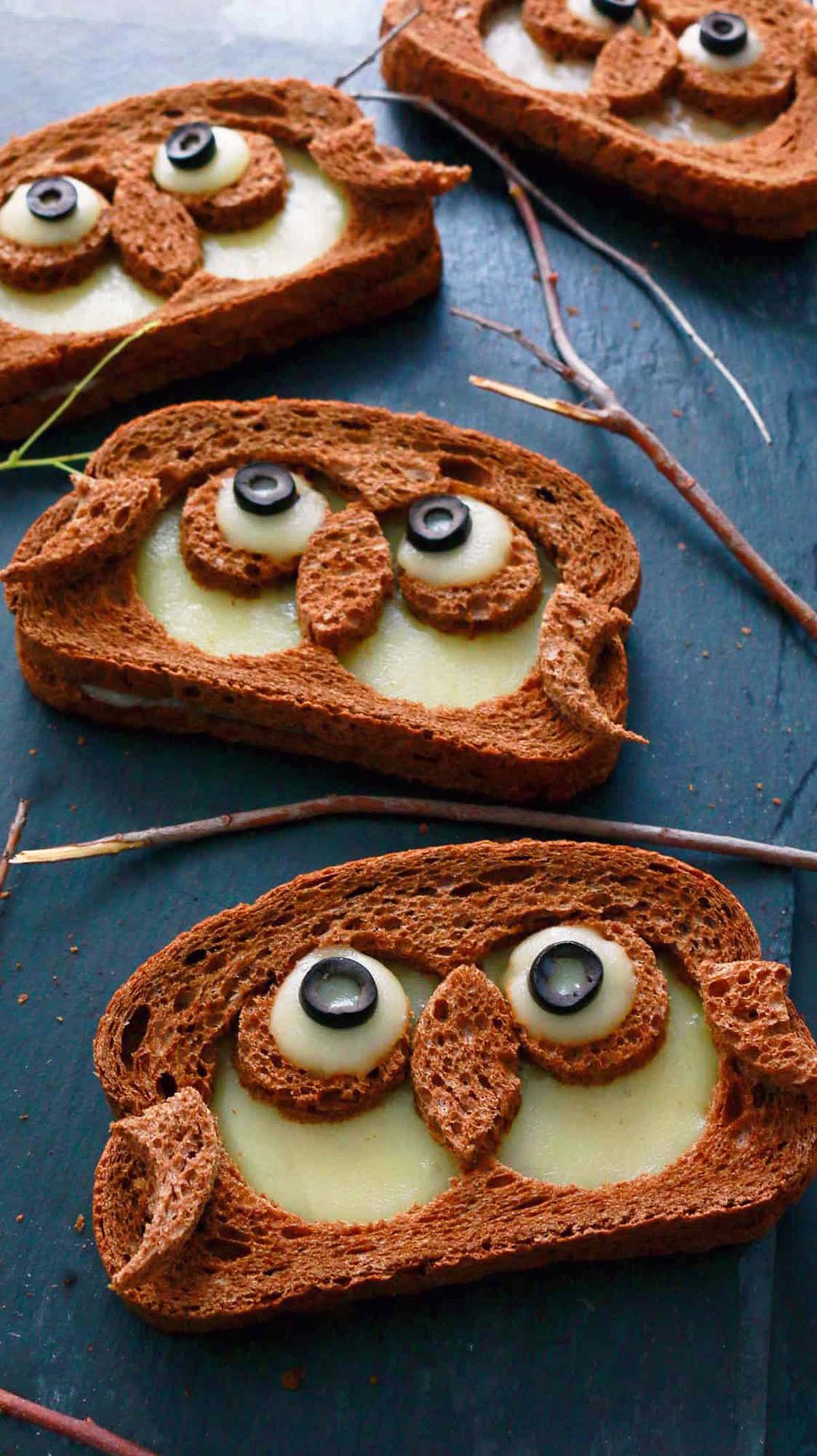 4 owl shaped grilled cheese sandwich placed on a black board.