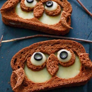 two sandwiches in the shape of owls on a black board.