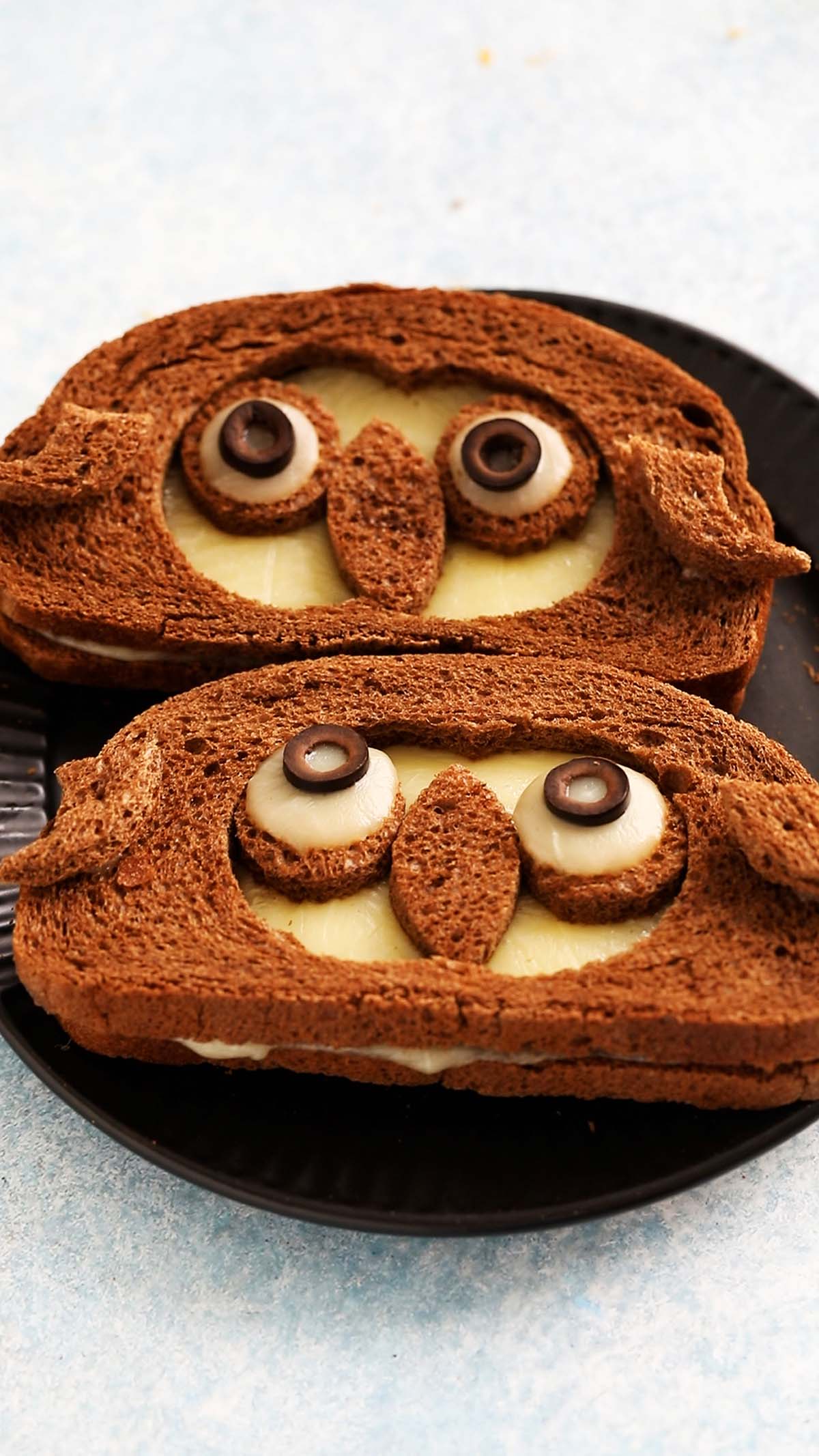 2 owl shaped sandwiches placed on a black plate.