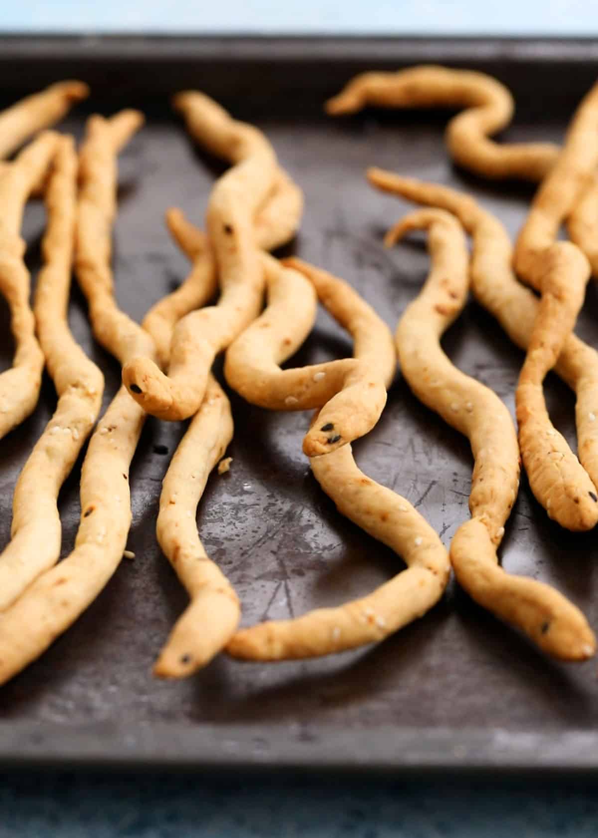 Snake shaped Halloween breadsticks on a black tray.