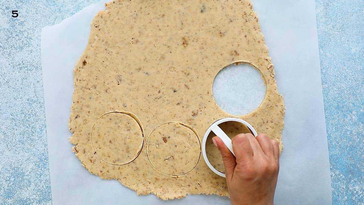 a hand cutting circles using a round cookie cutter from a cookie dough.
