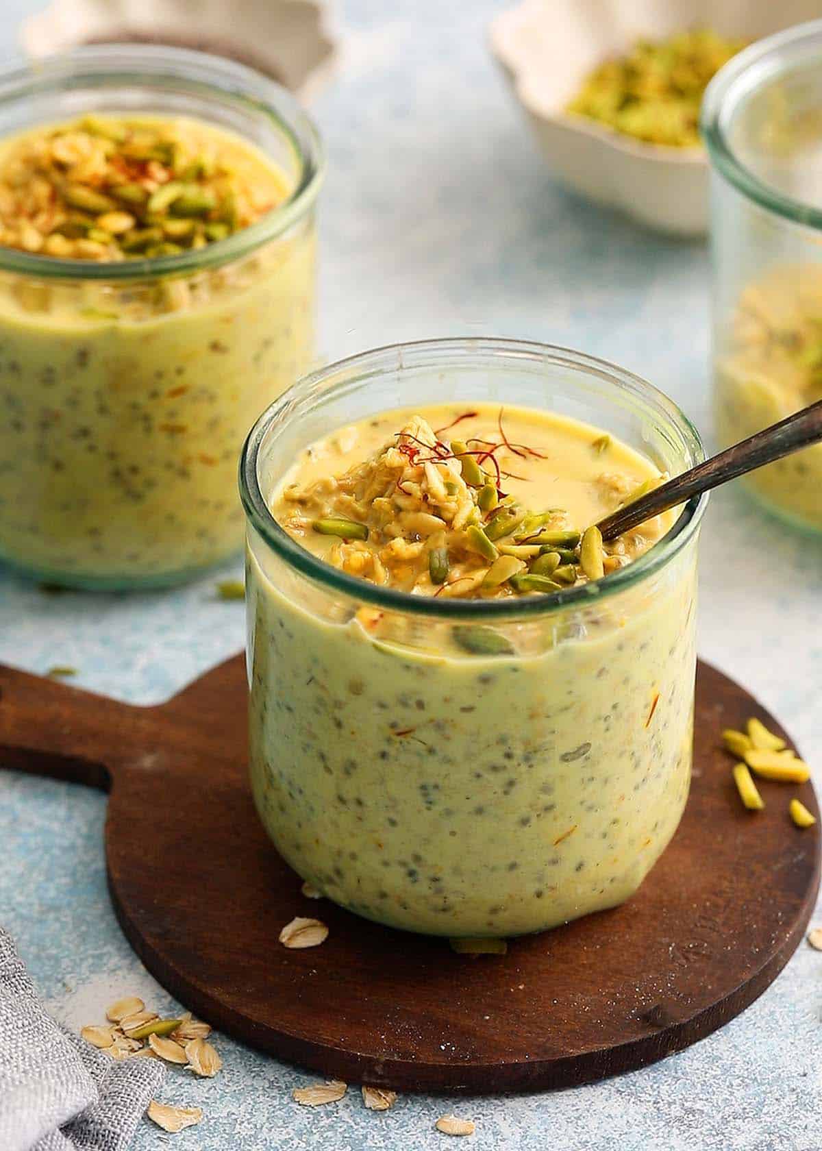 two glass jars filled with yellow colored overnight oats topped with green pistachios.