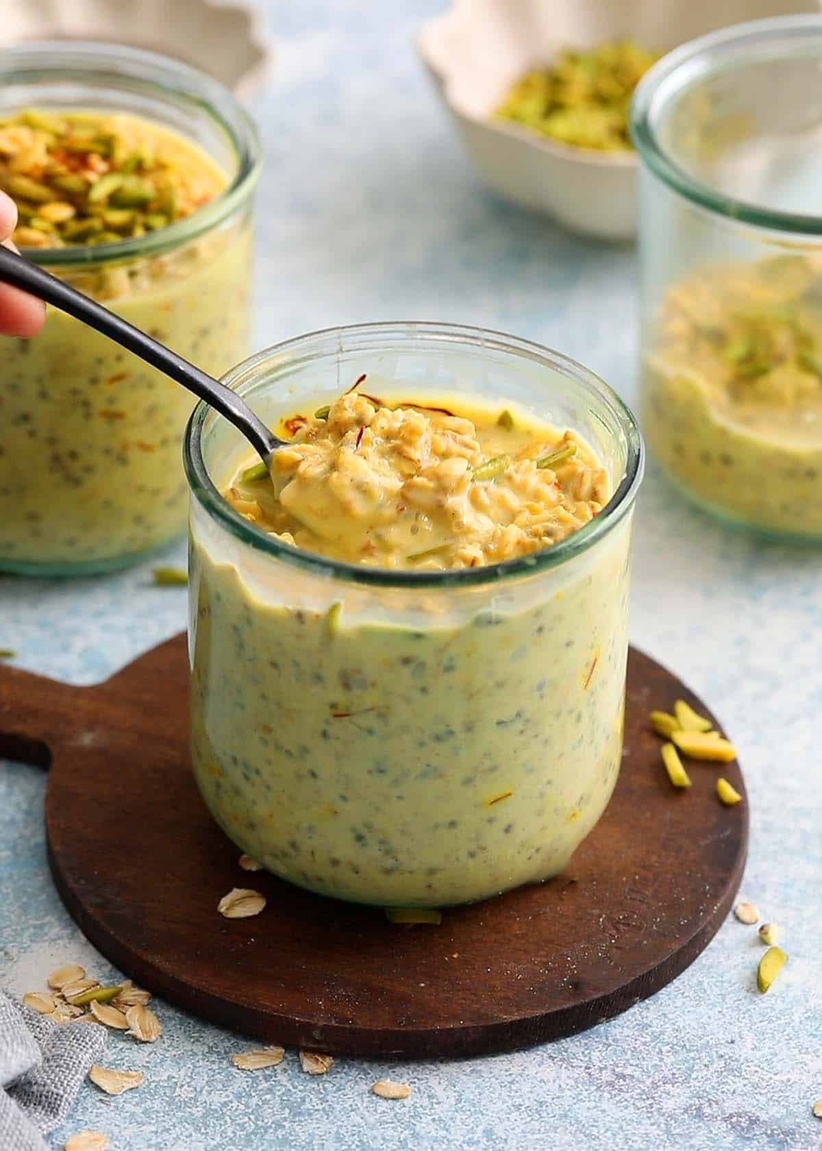 two glass jars filled with yellow colored overnight oats topped with green pistachios.