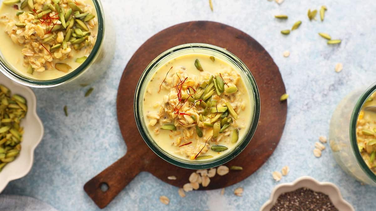 two glass jars filled with yellow colored overnight oats topped with green pistachios.