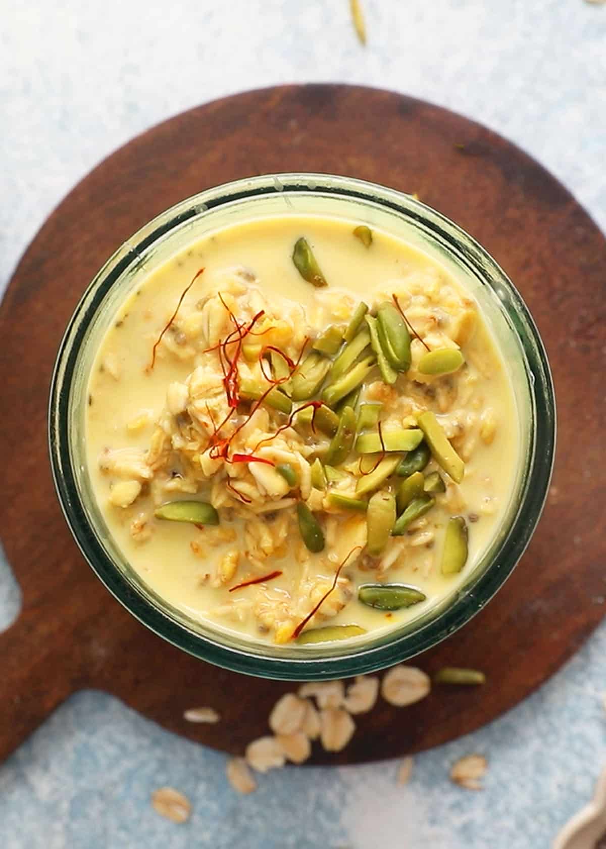 one glass jar filled with yellow colored overnight oats topped with green pistachios.