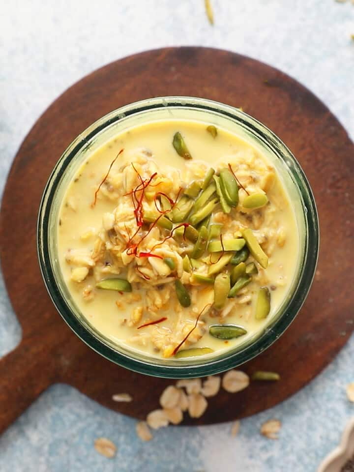 yellow overnight oats topped with green pistachios in a glass jar.