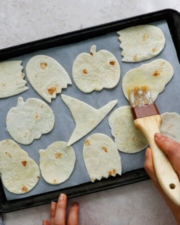 two hands brushing cut tortilla chips with melted butter using a brown brush.