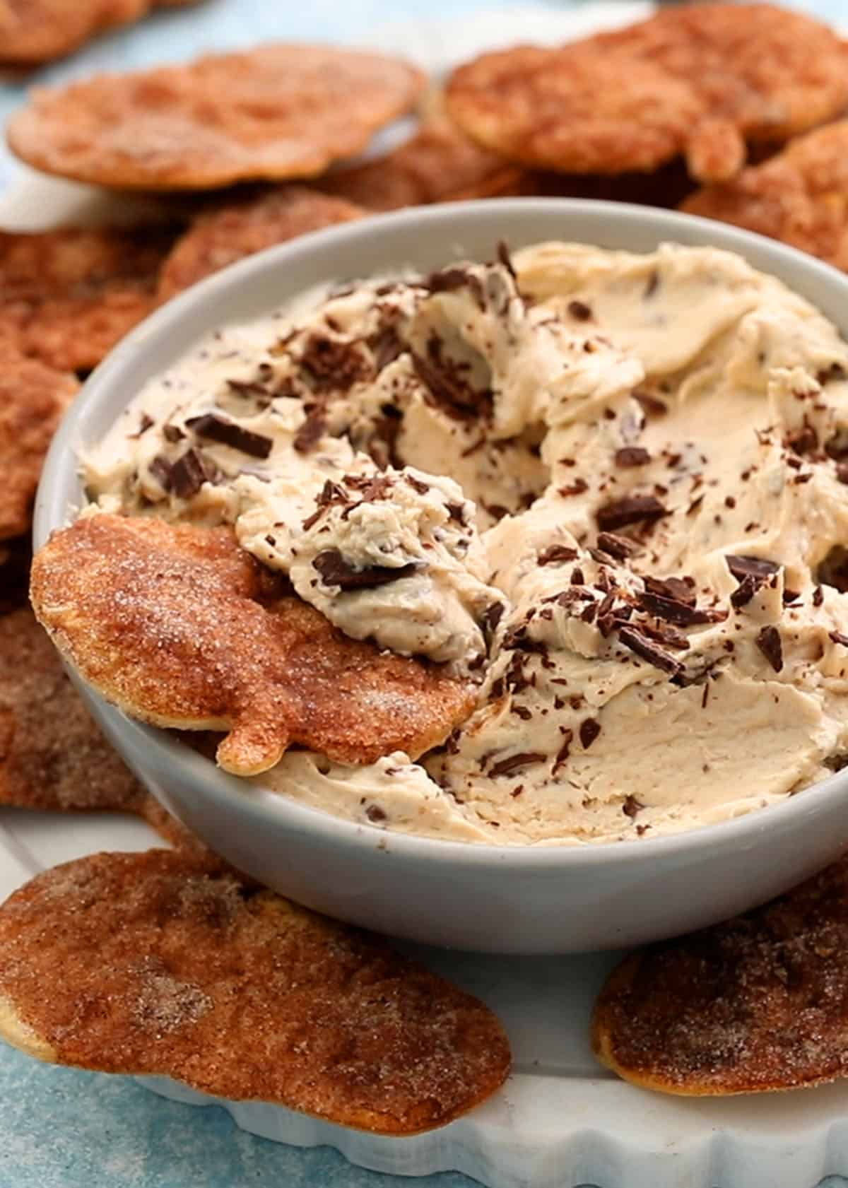 white cinnamon dip in a grey bowl with brown chips placed around it.