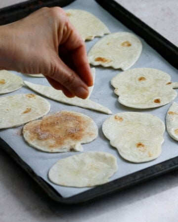 a hand sprinkling cut white tortilla shapes with brown cinnamon sugar.