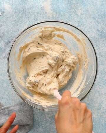 two hands mixing brown whipped cream in a glass bowl.