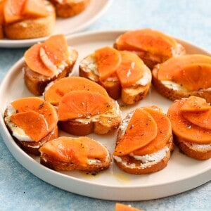 crostinis topped with persimmon in a white plate.